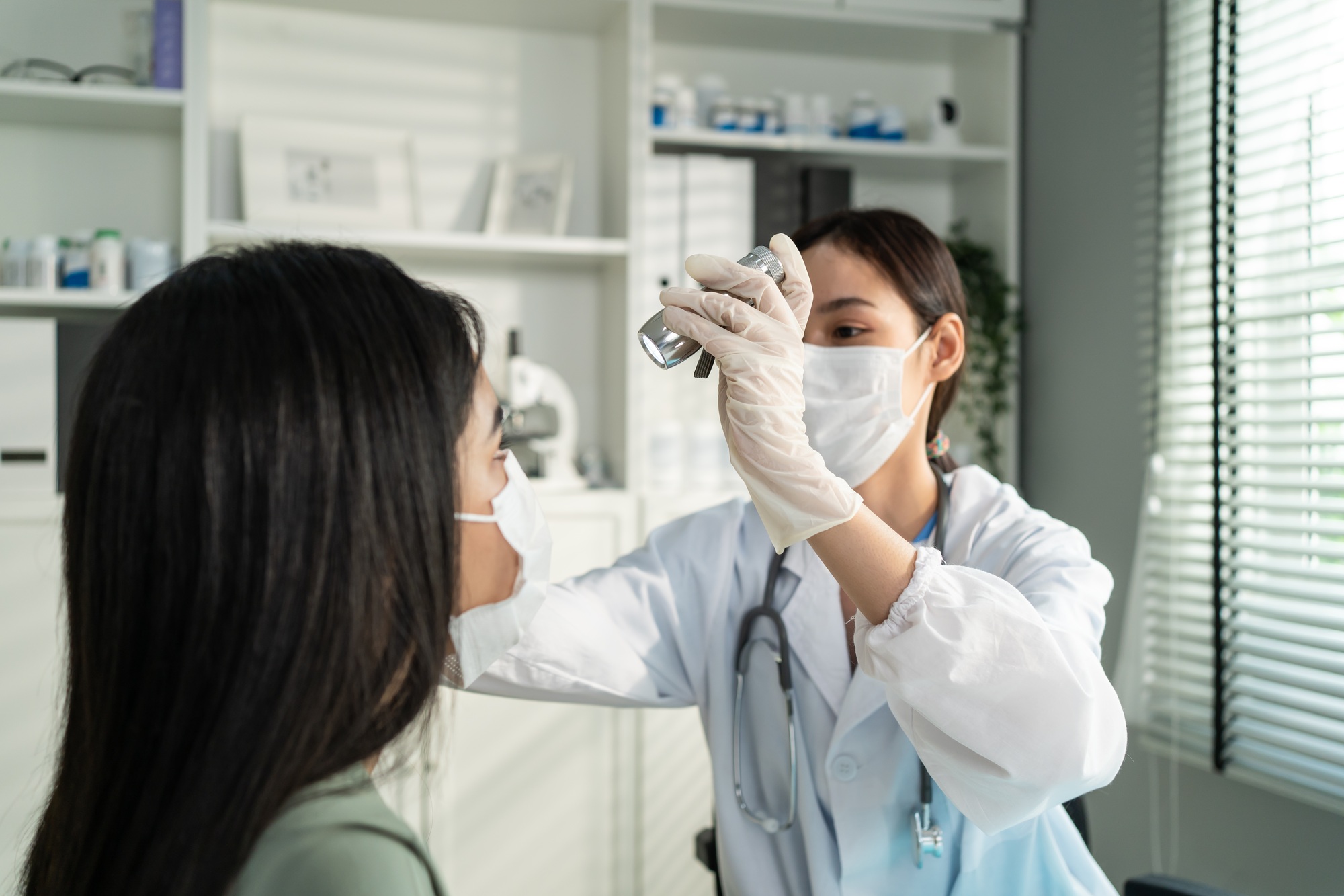 Asian young woman doctor using flashlight on patient's eye in hospital.