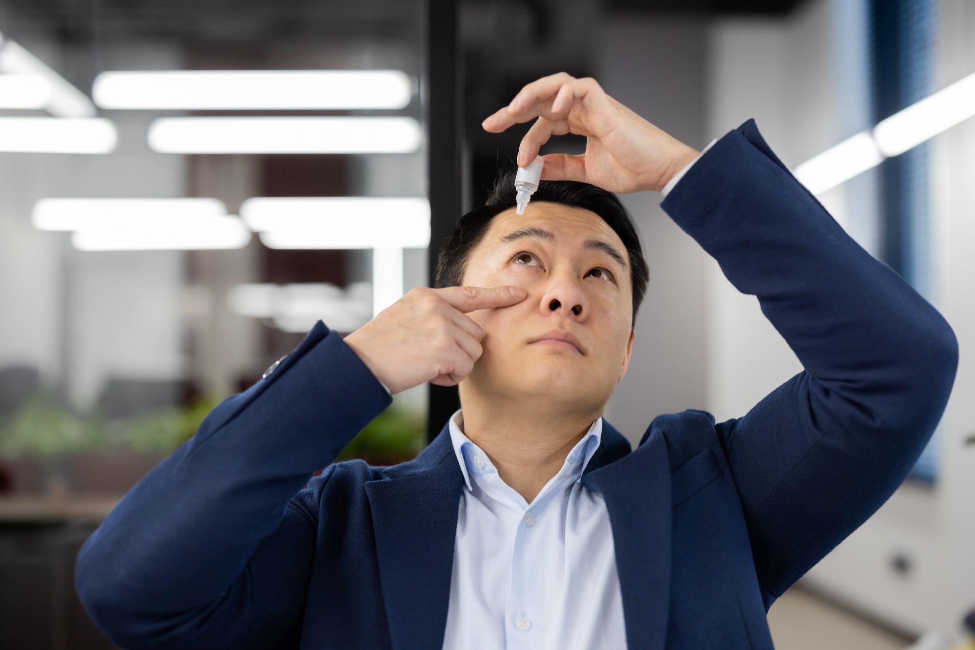 Close-up photo of a young Asian businessman who drips drops of medicine into his eye from overwork